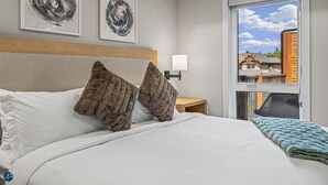 A hotel room with a large bed, two decorative wall art pieces, a window with a view of a building, and a nightstand with a lamp. - 3 bed/2 bath Sparrowhawk Resort-Topfloor-Sleeps 8 (Dead Man's Flats)