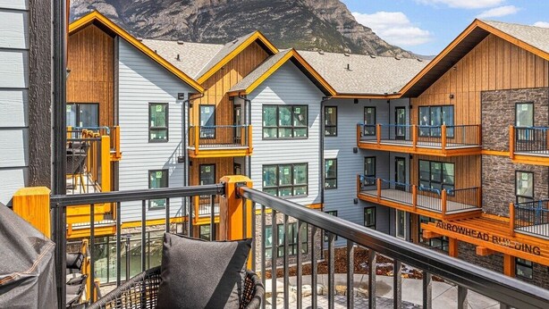 A multi-story building with balconies and large windows, set against a mountainous backdrop.