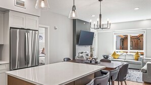 A modern kitchen with a large island, stainless steel refrigerator, and a dining area with chairs and a table.