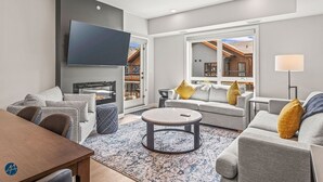 A modern living room with a flat-screen TV, grey sofas, a coffee table, and a patterned rug.