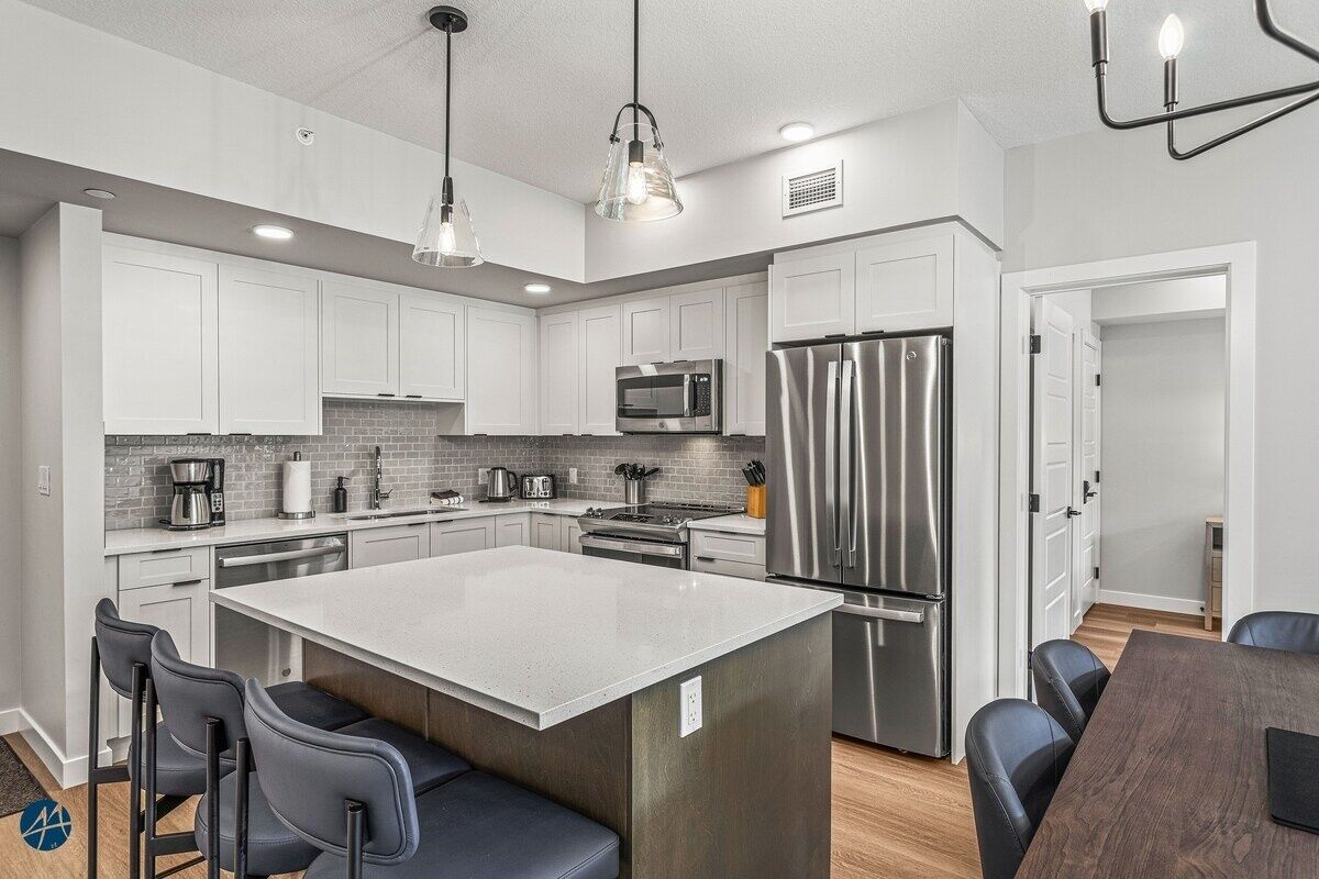 Una cocina moderna con armarios blancos, electrodomésticos de acero inoxidable y una isla central con asientos.