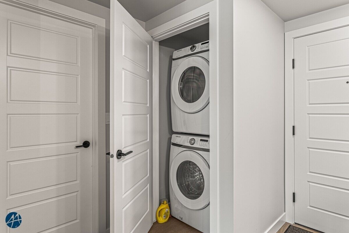 A laundry room with two stacked front-loading washing machines and a yellow detergent bottle on the floor.