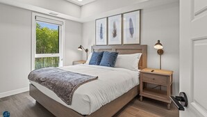 A modern bedroom with a large bed, two bedside tables, a window with a view of greenery, and framed artwork on the wall. - 2 Bed/2 Bath Sparrowhawk Resort-Sleeps 6 (Dead Man's Flats)