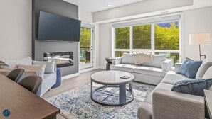 A modern living room with a fireplace, comfortable seating, and large windows offering a view of greenery. - 2 Bed/2 Bath Sparrowhawk Resort-Sleeps 6 (Dead Man's Flats)