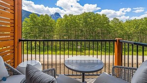 A balcony with wicker furniture and a table, overlooking a forest and mountains. - 2 Bed/2 Bath Sparrowhawk Resort-Sleeps 6 (Dead Man's Flats)