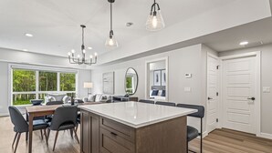 A spacious kitchen with a large island, modern pendant lights, and a dining area with a view of greenery.