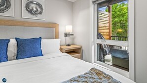 A modern hotel room with a large bed, a nightstand, a lamp, and a window with a view of greenery.