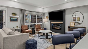 A modern living room with a sofa, chairs, a coffee table, a fireplace, a TV, and a large window with blinds.