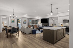 Una cocina moderna con una isla central, un comedor con mesa y sillas, una sala de estar con sofá y sillones, y un ventanal que ofrece vistas.