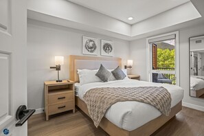 Une chambre moderne avec un grand lit, des tables de chevet en bois, une vue sur la verdure par la fenêtre et deux œuvres d’art accrochées au mur.