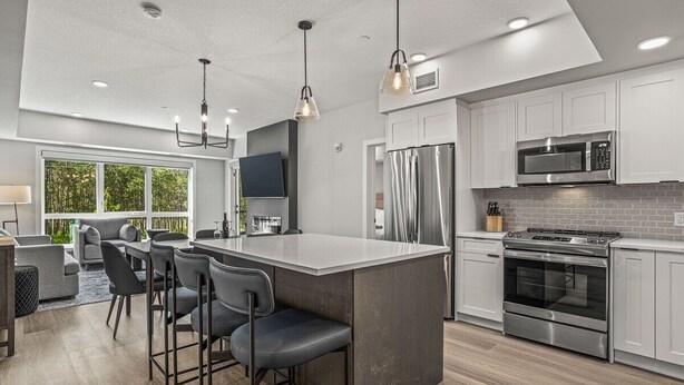 Una cocina moderna con una isla central, electrodomésticos de acero inoxidable y una zona de comedor con taburetes de bar.