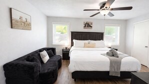 Une chambre à coucher avec un lit, un canapé noir, un ventilateur de plafond et un tableau accroché au mur.