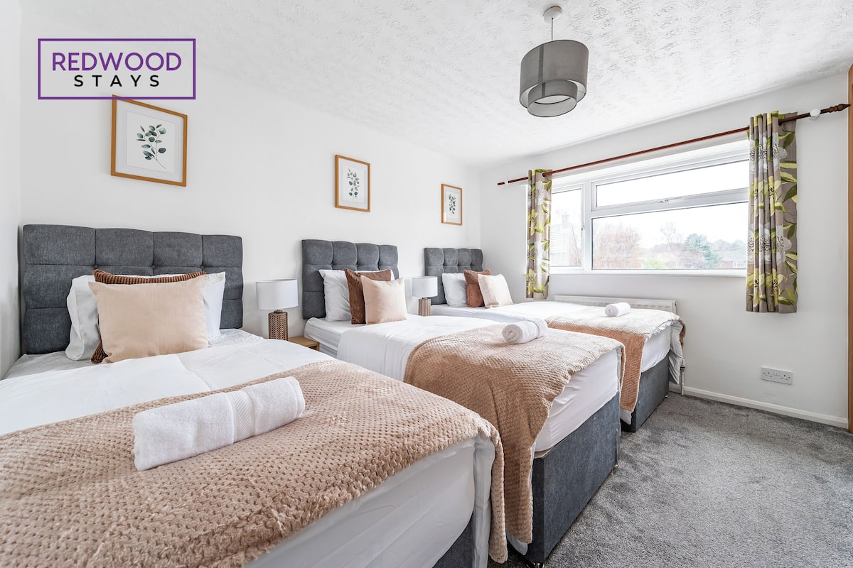 Habitación de hotel con tres camas, un ventanal con cortinas y una lámpara en el techo.