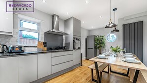 Een moderne keuken met grijze kastjes, een roestvrijstalen afzuigkap en een houten eettafel voor vier personen.