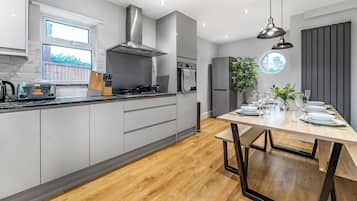 A modern kitchen with grey cabinets, a stainless steel range hood, and a wooden dining table set for four.