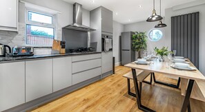 Una cocina moderna con armarios grises, una campana extractora de acero inoxidable y una mesa de comedor de madera dispuesta para cuatro personas.
