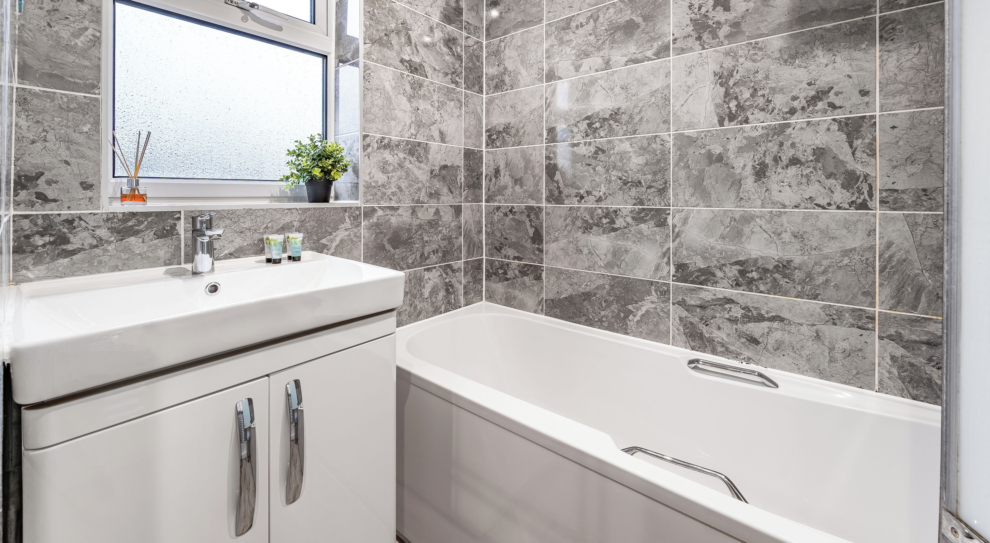 Ein modernes Badezimmer mit Wandverkleidung aus Marmorfliesen, einem weißen Waschbecken und einer Badewanne.