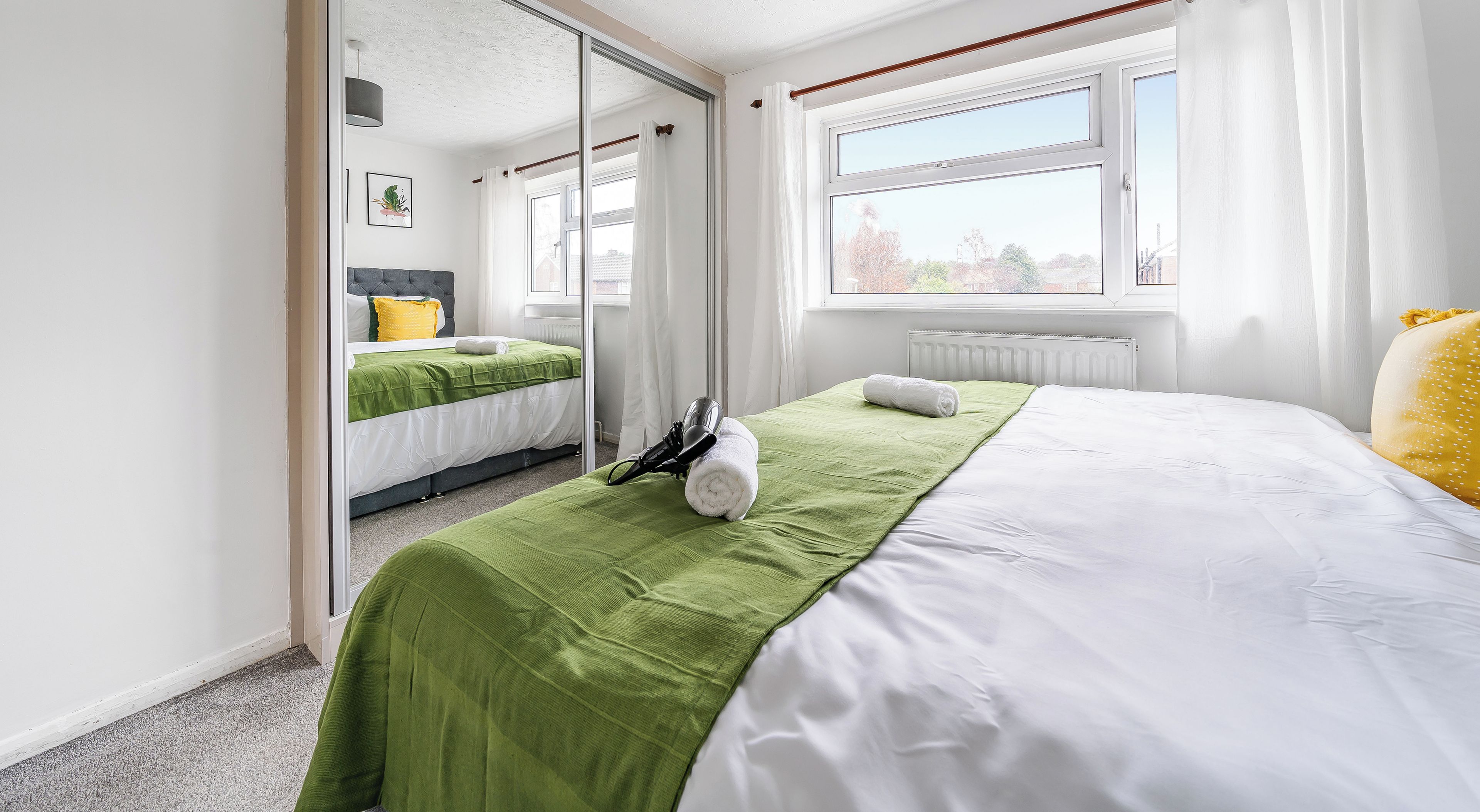 A hotel room with a large bed, a mirror, a window with curtains, and a radiator.