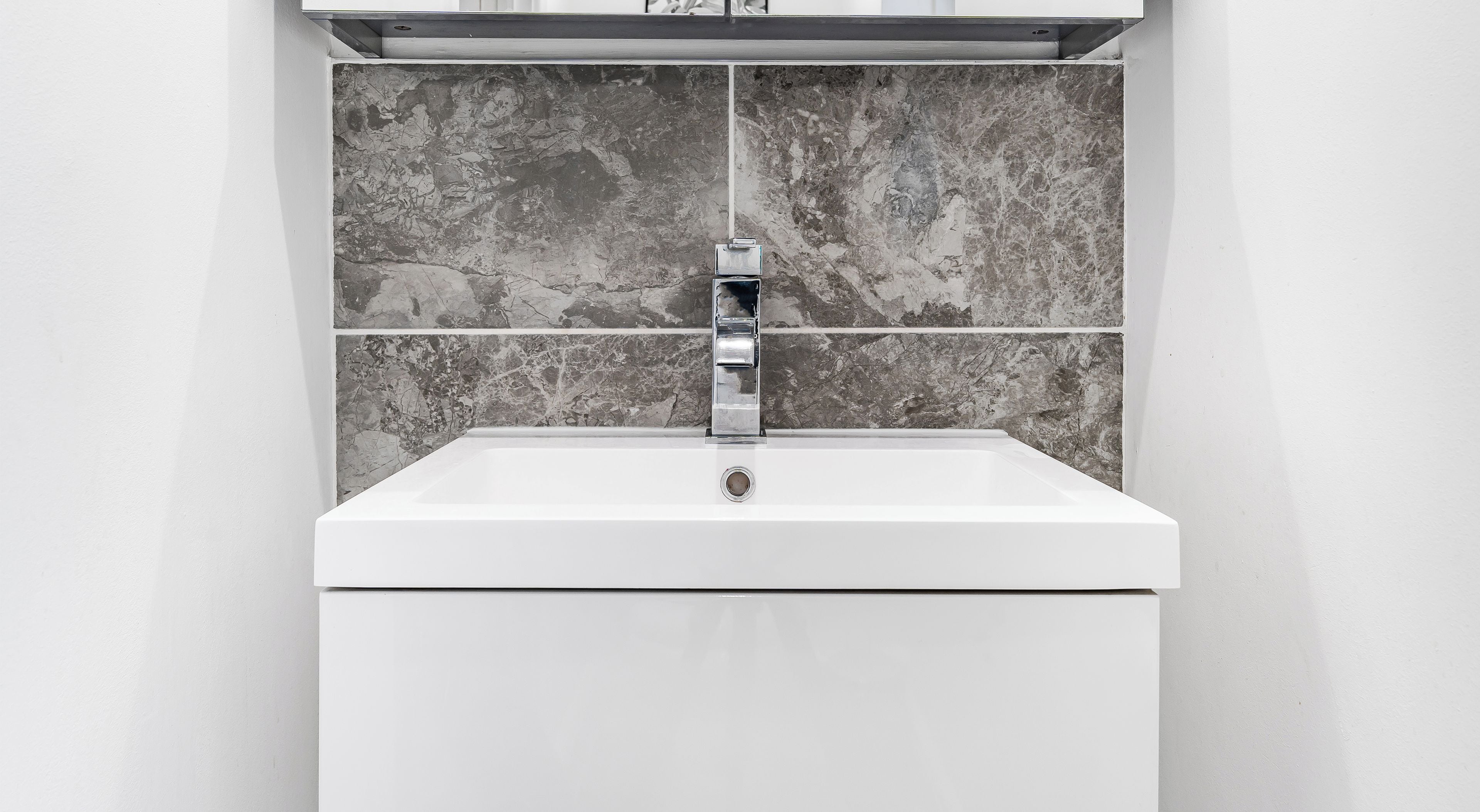 A modern bathroom with a white sink, a chrome faucet, and a marble backsplash.