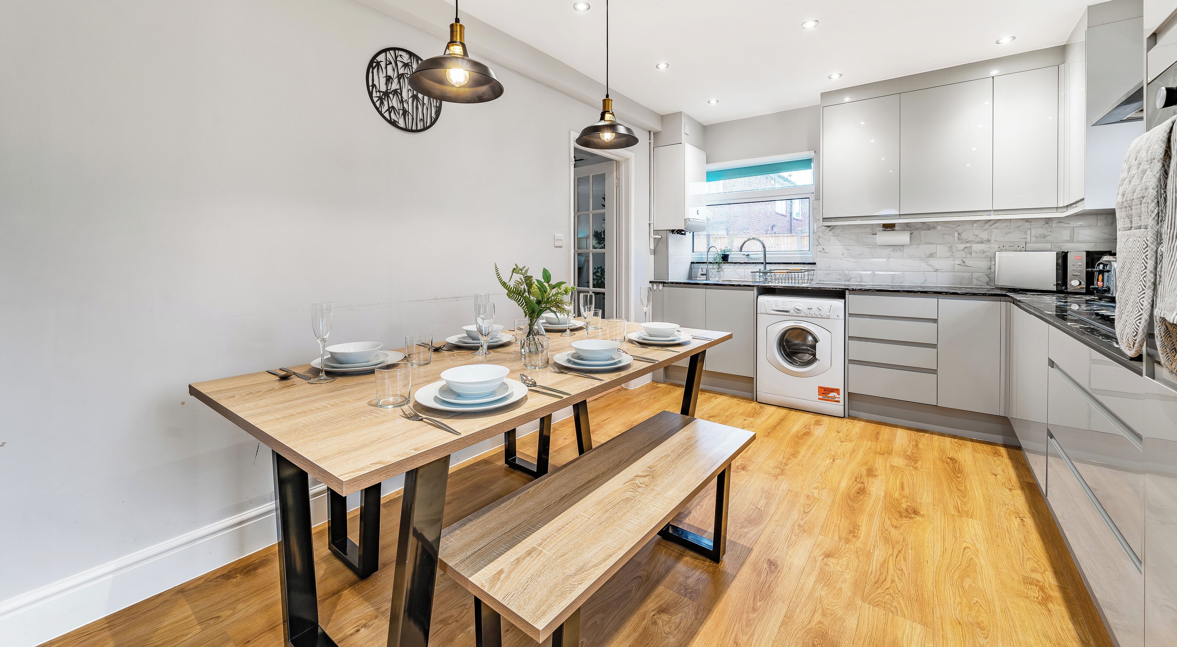 A modern kitchen with wooden flooring, a dining table set for four, and a washing machine.