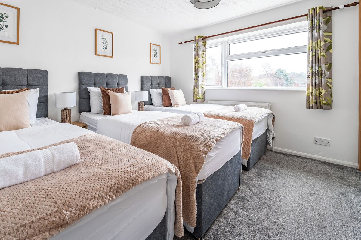 Habitación de hotel con tres camas, un ventanal con cortinas y una lámpara en el techo.