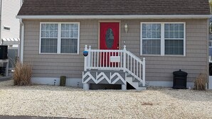 Una casa de dos pisos con una puerta roja, un pequeño porche con barandal blanco y un camino de entrada de grava.