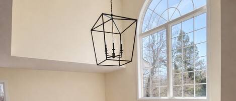 Un interior espacioso con techo alto, una escalera de madera, un amplio ventanal de arco y un candelabro colgante.