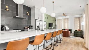 A modern kitchen with a long island, bar stools, and a dining area with a sofa and chairs. - 3-Level Lux Home! Rooftop! Firepit! 6 min to DT! (Nashville)