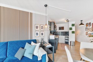 A modern living room with a blue sofa, a dining area with a white table, and a kitchen in the background. - Design Apartment Ludwigsburg (Ludwigsburg)