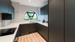 A modern kitchen with dark cabinetry, a white countertop, and a large window with a view of greenery.
