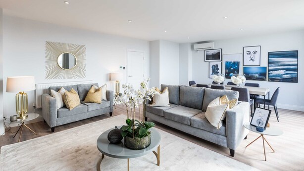 A modern living room with two grey sofas, a round coffee table, and a dining area with a white table and chairs.