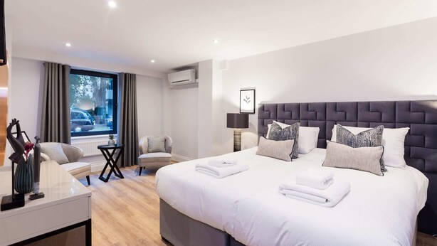 Ein modernes Hotelzimmer mit einem großen Bett, einem Schreibtisch, einem Sessel und Blick auf die Straße durch ein Fenster.
