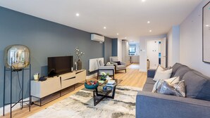 Ein modernes Wohnzimmer mit einer Couch, einem Couchtisch und einem Fernseher. Im Hintergrund befindet sich ein Essbereich.