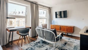 Ein modernes Hotelzimmer mit Schreibtisch, Stuhl, Fernseher und Blick auf Gebäude durch große Fenster.