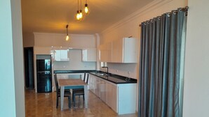 A modern kitchen with white cabinets, a black refrigerator, a dining table with chairs, and a large window with curtains. - Sea view  3-bedroom apartment in delightful hurghada , 
 with AC, WiFi (Red Sea Governorate)