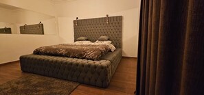 A bedroom with a tufted headboard, a large bed with a patterned bedspread, a matching ottoman, and a dark curtain. - Sea view  3-bedroom apartment in delightful hurghada , 
 with AC, WiFi (Red Sea Governorate)