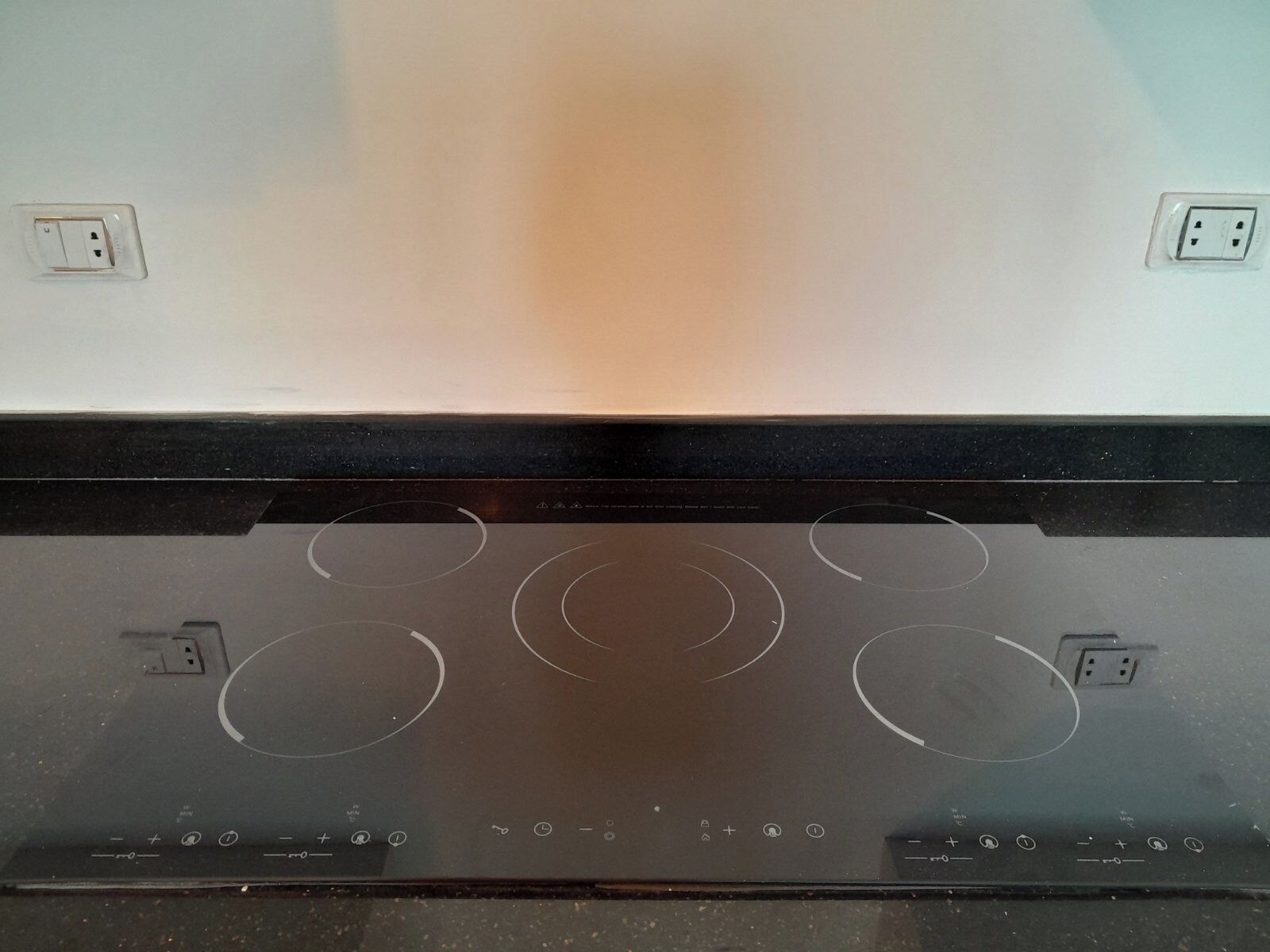 A kitchen with a black stovetop and two electrical outlets on the wall.