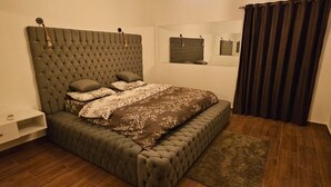 A bedroom with a tufted headboard, a bed with patterned bedding, a bedside table, a mirror, and dark curtains. - Sea view  3-bedroom apartment in delightful hurghada , 
 with AC, WiFi (Red Sea Governorate)