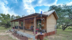 A wooden cabin with a porch, outdoor seating, and a rustic aesthetic. - ‘Cozy Cabin’ Hill Country Escape w/ Views (Johnson City)