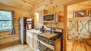 A wooden cabin kitchen with a refrigerator, stove, microwave, and wooden cabinets. - ‘Cozy Cabin’ Hill Country Escape w/ Views (Johnson City)