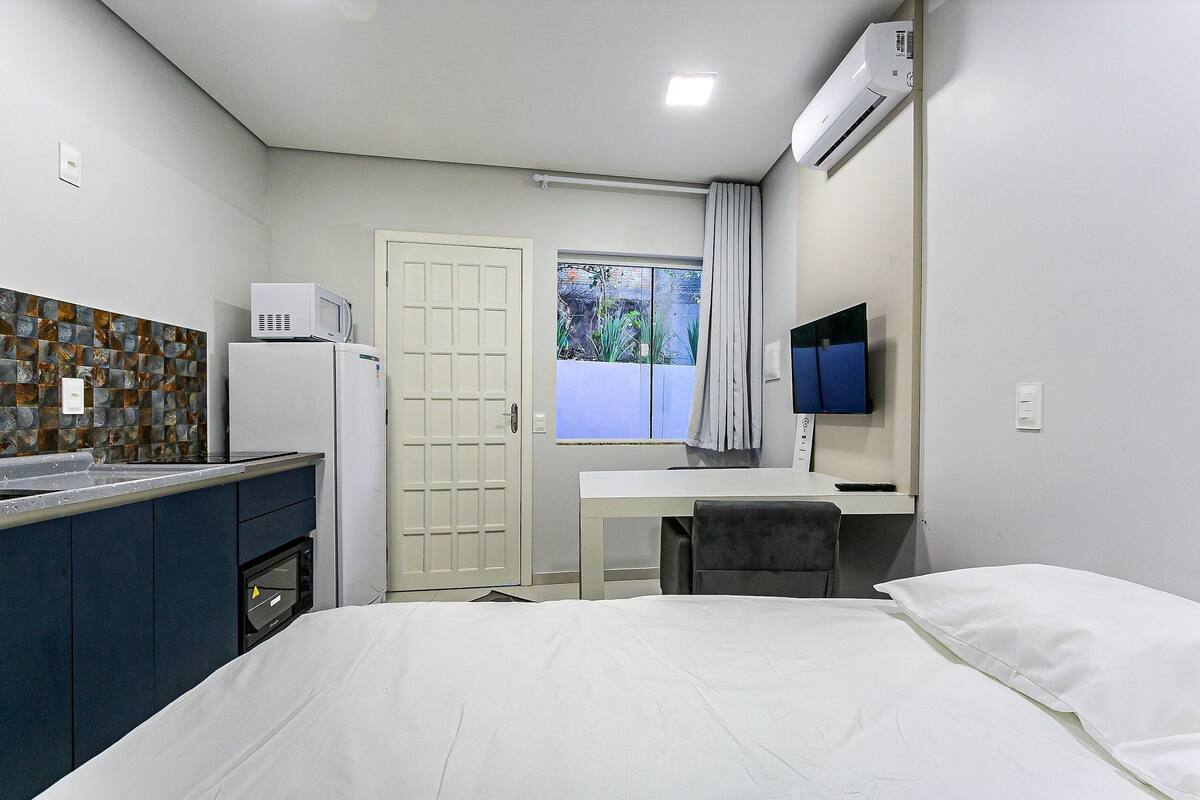 Habitación de hotel pequeña con cama, escritorio, televisión, microondas y kitchenette.
