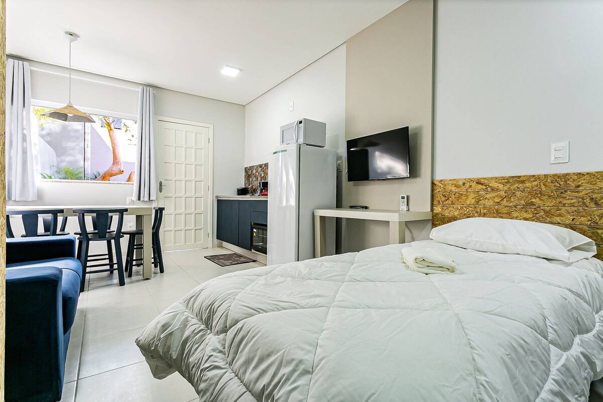 Habitación de hotel con cama, escritorio, silla, televisión y vistas al exterior.