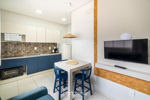 Cocina compacta con microondas, tostadora y refrigerador. Hay una mesa de comedor con sillas y un televisor montado en la pared.
