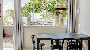 Un coin repas avec une table et des chaises, une vue sur la mer grâce à de grandes fenêtres et une plante suspendue.