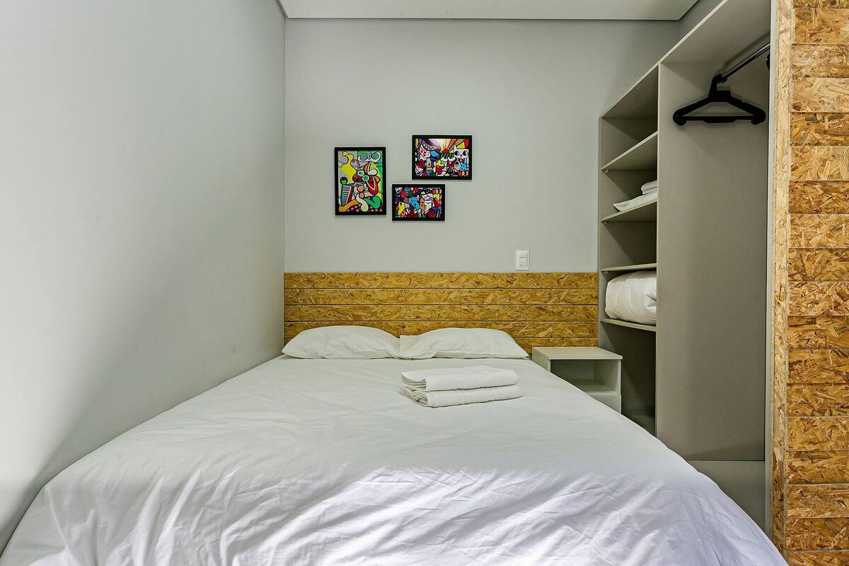 Una cama bien hecha con sábanas blancas, un cabecero de madera y una pared con tres obras de arte coloridas.