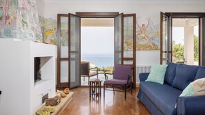 Un salon avec un canapé bleu, un fauteuil violet et une table basse en bois. On y trouve une cheminée agrémentée d’objets décoratifs et une grande fresque murale.