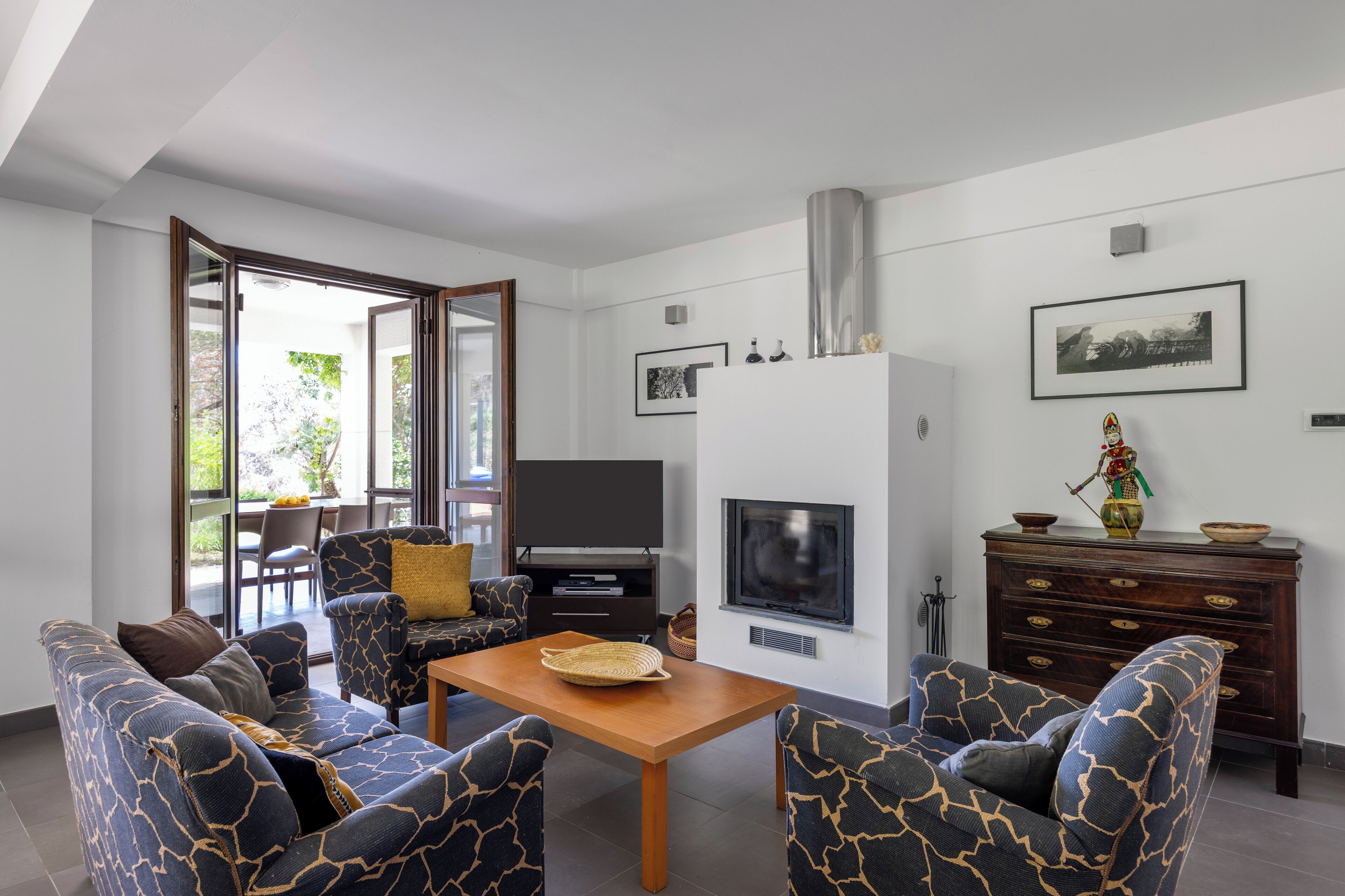 A modern living room with a sofa set, a wooden coffee table, a flat-screen TV, a fireplace, and a dining area with a table and chairs.