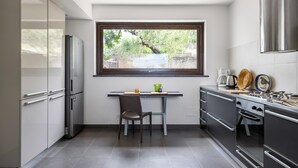 Une cuisine compacte dotée d’un réfrigérateur intégré, d’une table à manger avec deux chaises et d’une fenêtre donnant sur un espace verdoyant.