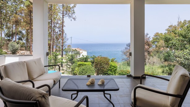 Un balcon avec vue sur la mer, deux chaises et une table agrémentée de deux coquillages décoratifs.