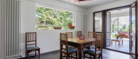 A dining area with a wooden table and chairs, a window with a view of greenery, and a decorative ceiling light.